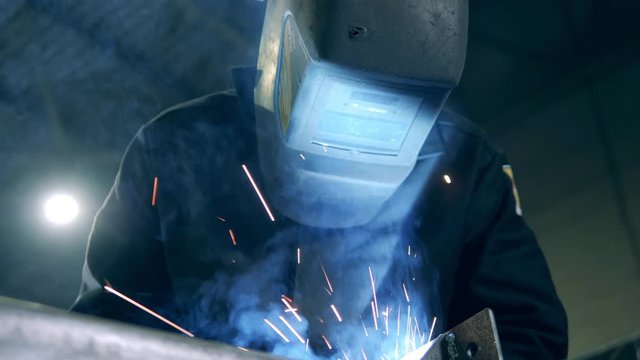 Professional welder in a helmet and sparks caused by welding