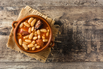 Typical Spanish fabada asturiana in crockpot on wooden table. Top view. Copy space