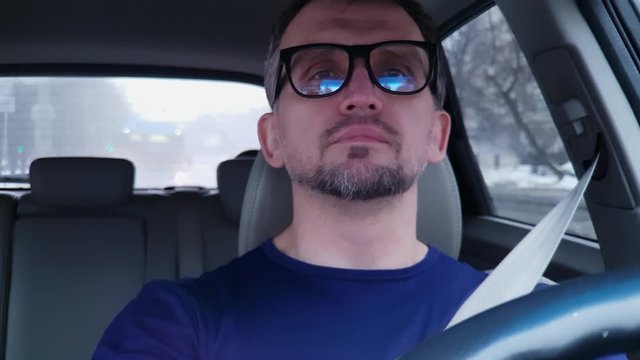 White bearded man with glasses drives car, parks and takes off his glasses