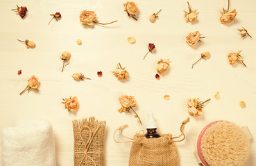 Set of natural soap, aroma oil, white towel and body brush with dried rose buds as a decoration on wooden background.