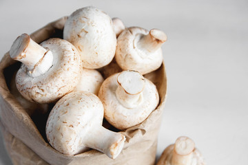 Mushrooms champignons in paper bag on a white wooden table. Close up. Place for text or advertising