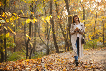 Image of young woman using smartphone while walking in autumn park