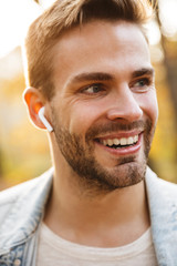Fototapeta premium Image of handsome young caucasian man using earbuds while walking in park