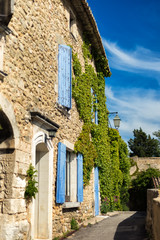 Vertical picture of traditional medieval stone provencal house with blue shutters and ivy on walls in sunny day in Menerbes, one of most beautiful villages of France in heart of Provence. Travel