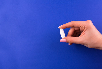  One suppository for anal or vaginal use in a female hand on a blue background. Medical candles....