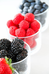 Assortment of fresh berries on a white background. Raspberries, blueberries, blackberries, strawberries in small glasses. Healthy eating. Vegan food. 