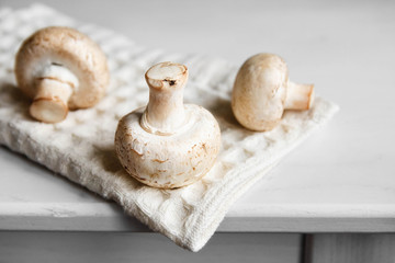 Mushrooms champignons on the kitchen napkin on a white wooden table. Place for text or advertising