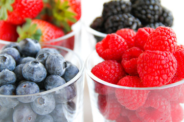 Assortment of fresh berries on a white background. Raspberries, blueberries, blackberries, strawberries in small glasses. Healthy eating. Vegan food. 