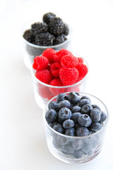 Assortment of fresh berries on a white background. Raspberries, blueberries, blackberries, strawberries in small glasses. Healthy eating. Vegan food. 
