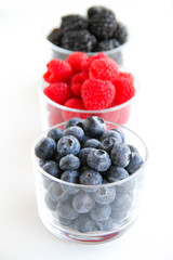 Assortment of fresh berries on a white background. Raspberries, blueberries, blackberries, strawberries in small glasses. Healthy eating. Vegan food. 