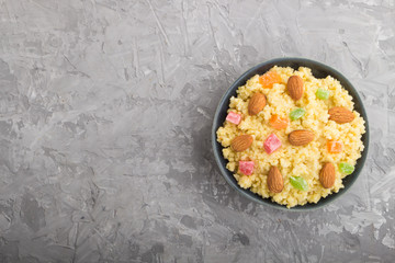 Millet porridge with candied fruits and almonds in blue ceramic bowl on a gray concrete background. Top view, copy space.