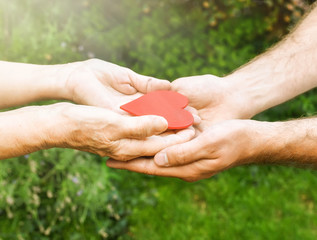 Hands with a red heart closeup.Young man gives a red heart to elderly woman. Human emotions, old...