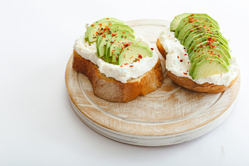 Two avocado toasts, avocado sandwich. Fresh avocado sliced on toast of wheat bread, cream cheese. Avocado sprinkled with chili, basil spices on a white background with place for text, top view.