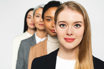 selective focus of four attractive and multicultural businesswomen looking at camera isolated on white