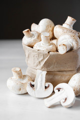 Mushrooms champignons in paper bag on a white wooden table. Place for text or advertising