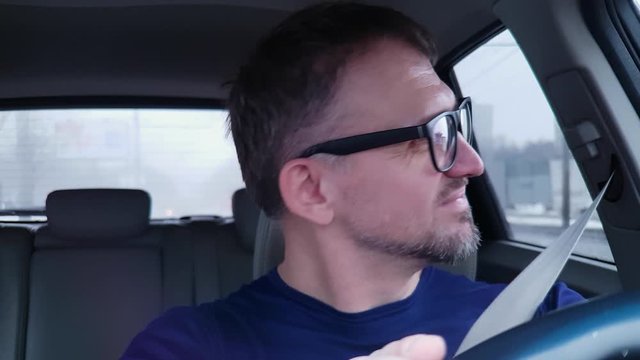 Caucasian man drives passenger car, smiles, nod to music. Very strong reflection in his glasses