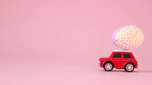 Red toy car model with a golden egg on the hood on a pink background. Gift delivery. Happy easter concept