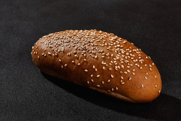 Fresh, delicious baked bread sprinkled with white sesame seeds against black background with copy space. Rural cuisine or bakery. Close-up