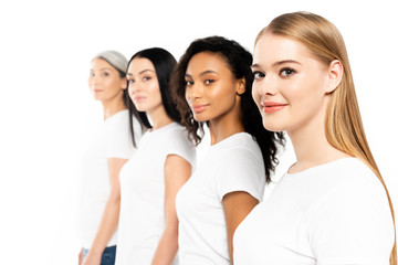 selective focus of four multicultural women in white t-shirts looking at camera isolated on white
