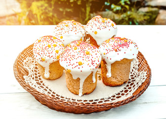 Happy Easter cake with sprinkles on white glaze. Cake on white rustic board, lace cloth, blur green plants and sun. Homemade bakery, spring holiday preparation. Selective focus, free text space.
