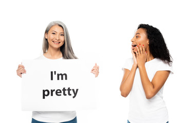 cheerful african american and asian women near i`m pretty placard isolated on white