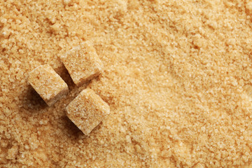 Brown sugar cubes on sugar background, space for text