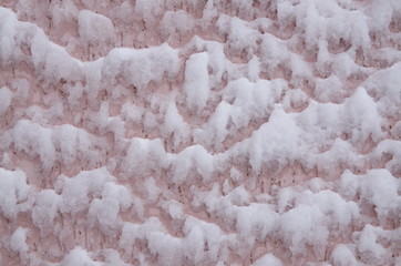Backgrounds and textures. On the wall, covered with pink stucco, white fluffy snow has stuck.