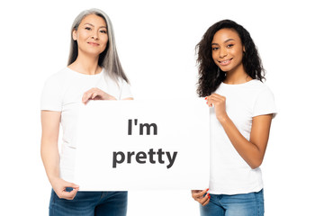 happy african american and asian women holding i`m pretty placard isolated on white