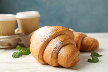 Tasty croissants and cups with coffee on wooden background, close up