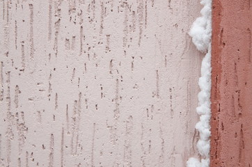 Backgrounds and textures. On the wall, covered with pink stucco, white fluffy snow has stuck.