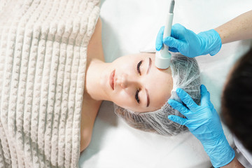 Microcurrent therapy for facial care. Cosmetologist doing face rejuvenation treatment. View above.
