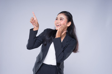 An attractive woman wearing business attire with gestures towards copyspace area isolated on grey....