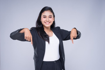 An attractive woman wearing business attire with gestures towards copyspace area isolated on grey....