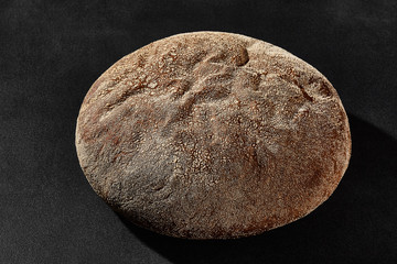 Fresh, tasty baked round dark bread sprinkled with flour. Black background with copy space. Rural cuisine or bakery. Close-up