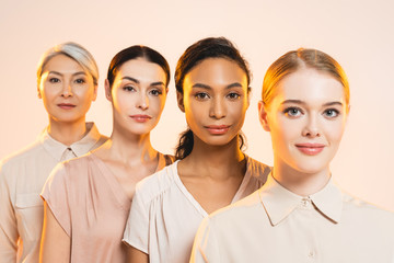 selective focus of happy multicultural women looking at camera isolated on beige
