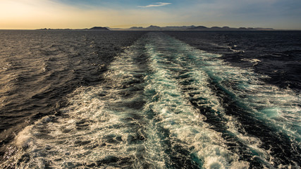 espuma en el mar por el barco con cielo azul e isla al fondo