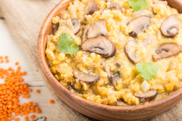 Lentils porridge with champignons. and coriander in a wooden bowl on a white wooden background. Side view, selective focus.