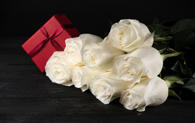 .bouquet of white roses and a gift on a black background