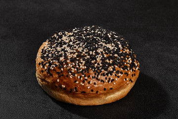 Fresh, palatable baked bun sprinkled with sesame seeds against black background with copy space. Rural cuisine or bakery. Close-up