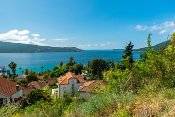 Seascape with tiled roofs of houses, yachts and forest. On a sunny day with blue sky.