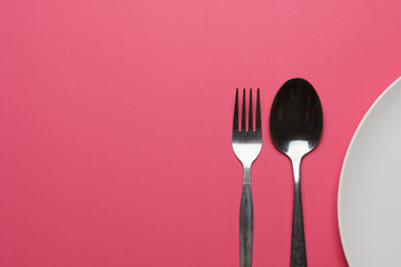dieting and health care concept. top view of a fork, spoon and plate on pink dine table. flat lay. free copy space for your text