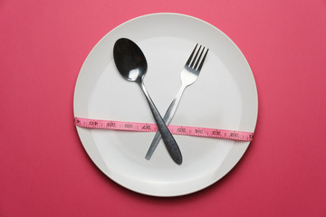 dieting and health care concept. top view of a fork, spoon and plate with measure tape on pink dine table. flat lay. free copy space for your text