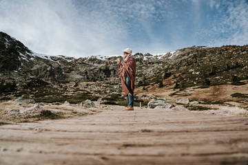 .Young and relaxed woman enjoying a sunny winter day in the mountains using a blanket. Carefree, free and calm. Lifestyle.