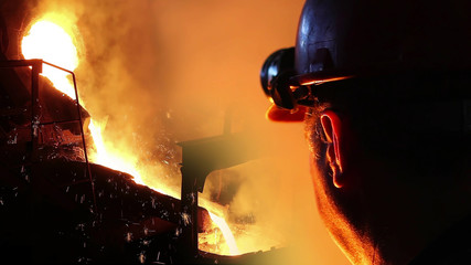 Liquid metal in the foundry, melting iron in furnace, steel mill. Worker with goggles and helmet controlling iron smelting in furnaces, applying heat to ore in order to extract a base metal