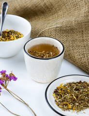 A cup of herbal tea with various herbs on a white background