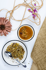 A cup of herbal tea with various herbs on a white background