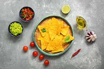 Traditional mexican snack nachos in a plate with guacamole and salsa sauce on a gray concrete background. Top view, flat lay, copy space.