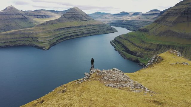 Flying around a hiker at the top of a mountain above Funningur on Faroe Islands