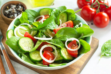 Diet menu. Healthy vegetable salad of fresh tomato, cucumber, onion and spinach on slate, stone or concrete background.