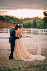 Two lovers black man and white woman stand embracing on a ranch at sunset